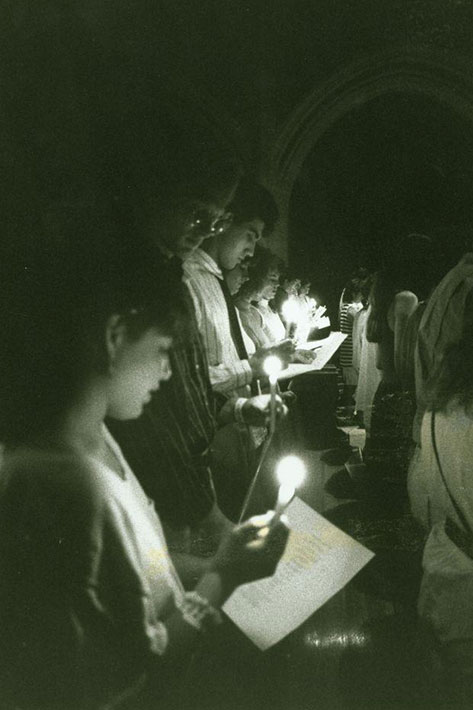 Students faces are light by candlelight in a church in a black and white image.