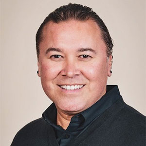 A photo headshot of an adult smiling while wearing a black collared shirt.